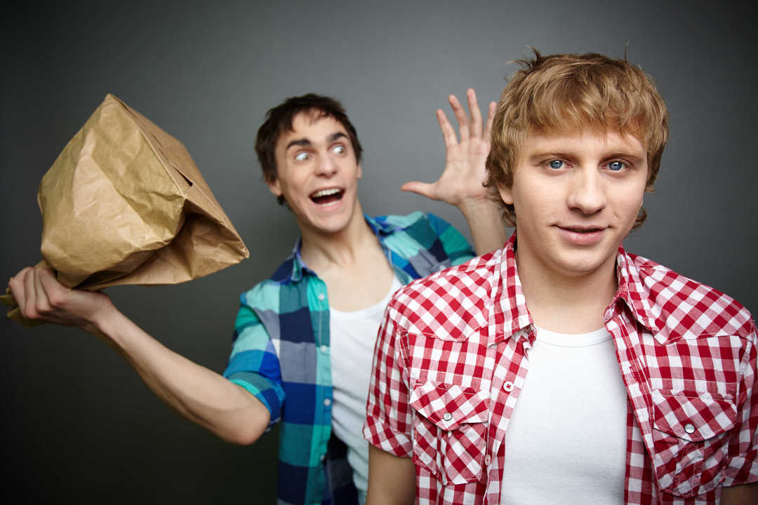 Crazy guy being ready to explode paper bag behind his friend back