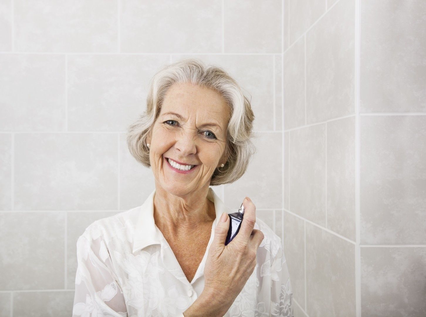 Portrait of happy senior woman spraying perfume in bathroom