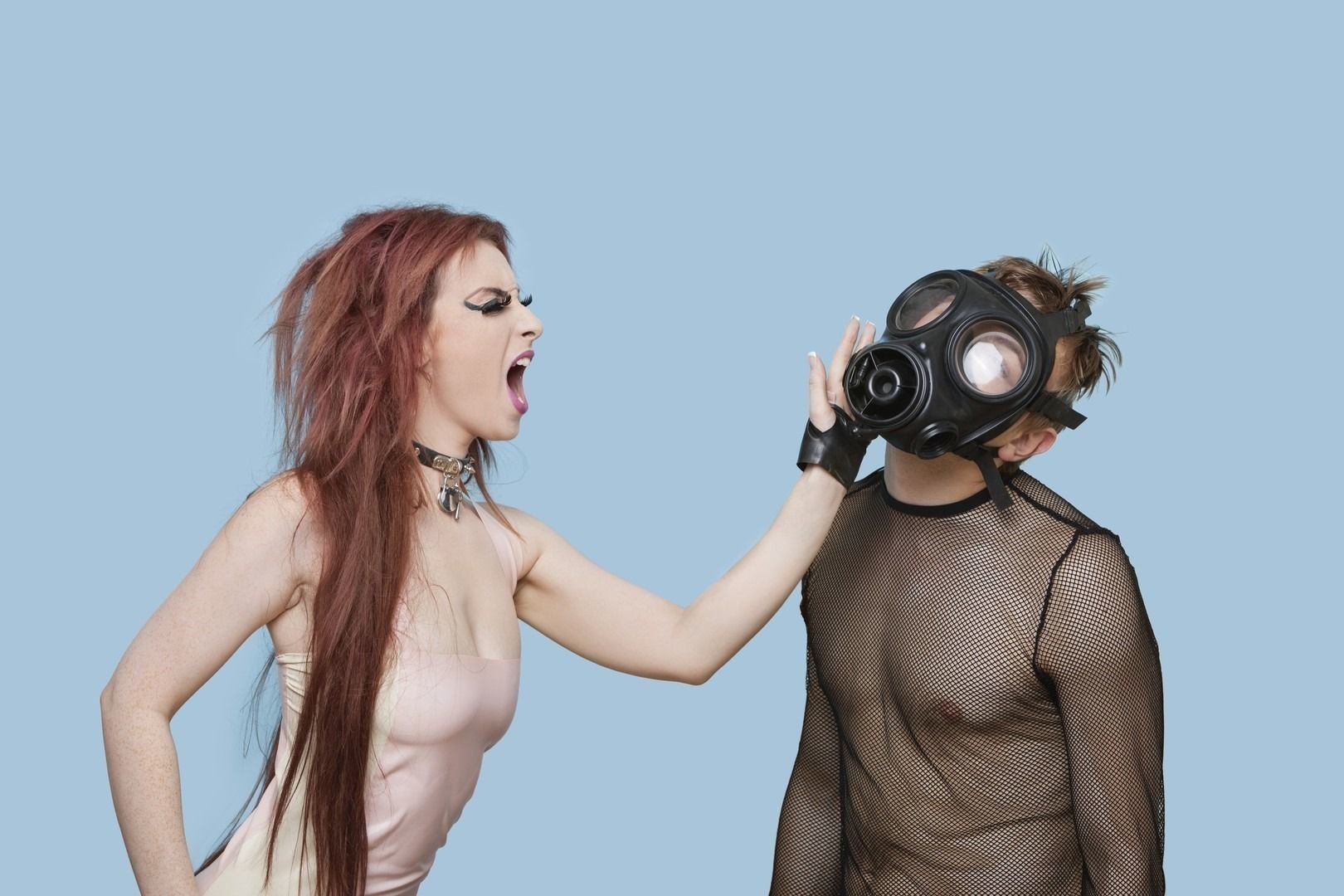 Funky young woman slapping man in gas mask over blue background