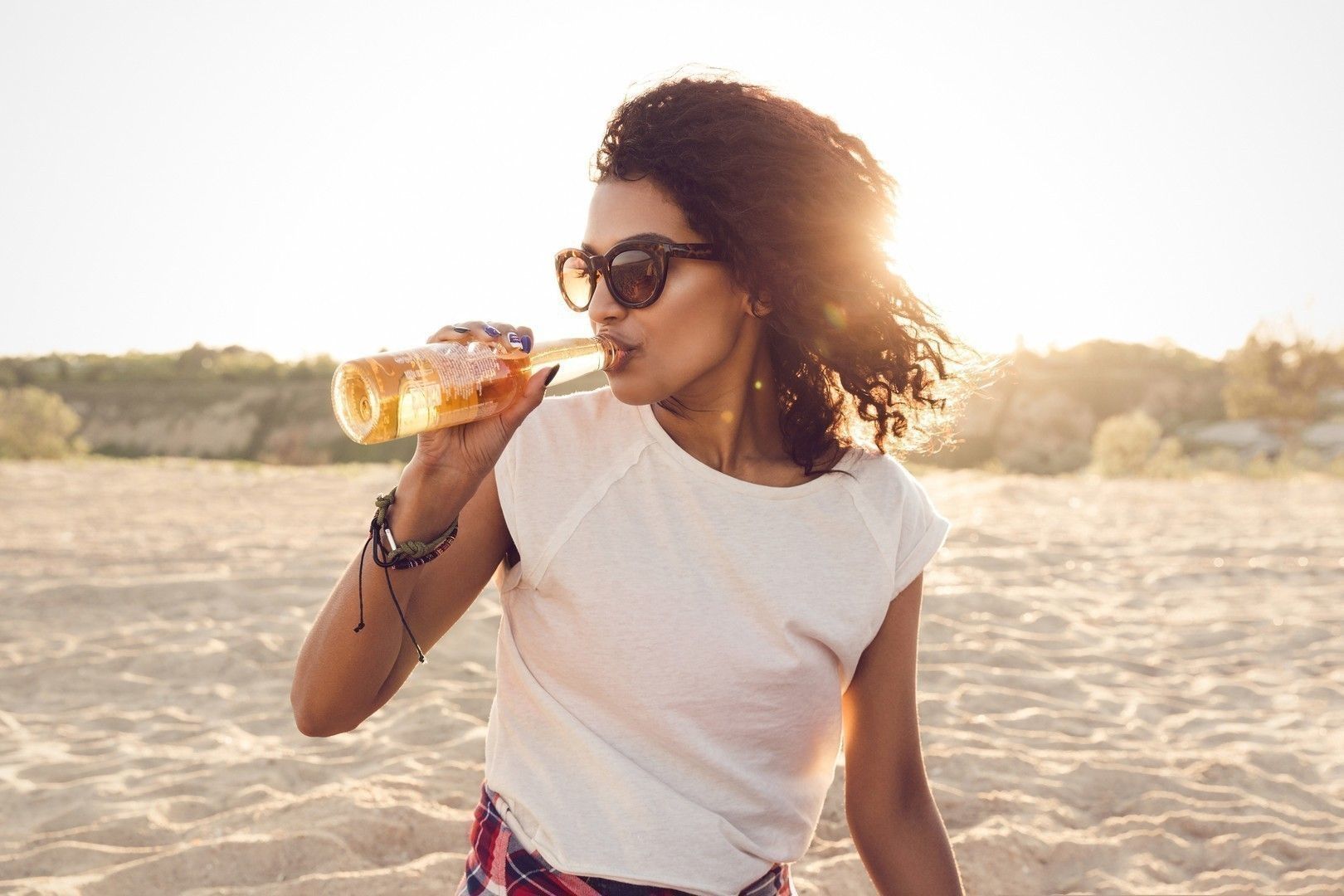 Young pretty african girl in sunglasses drinking beer