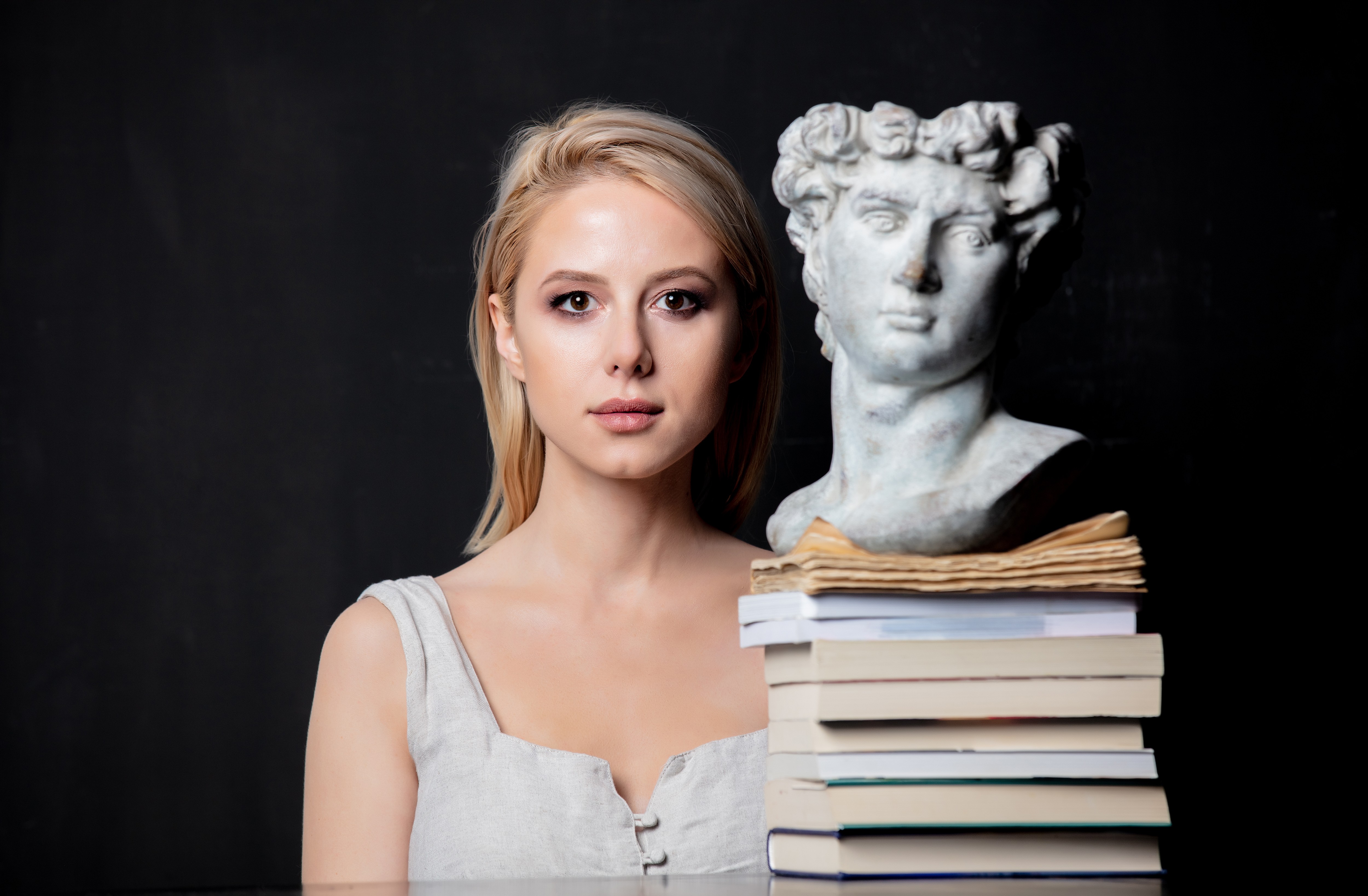 blonde next to an antique bust of a man on books